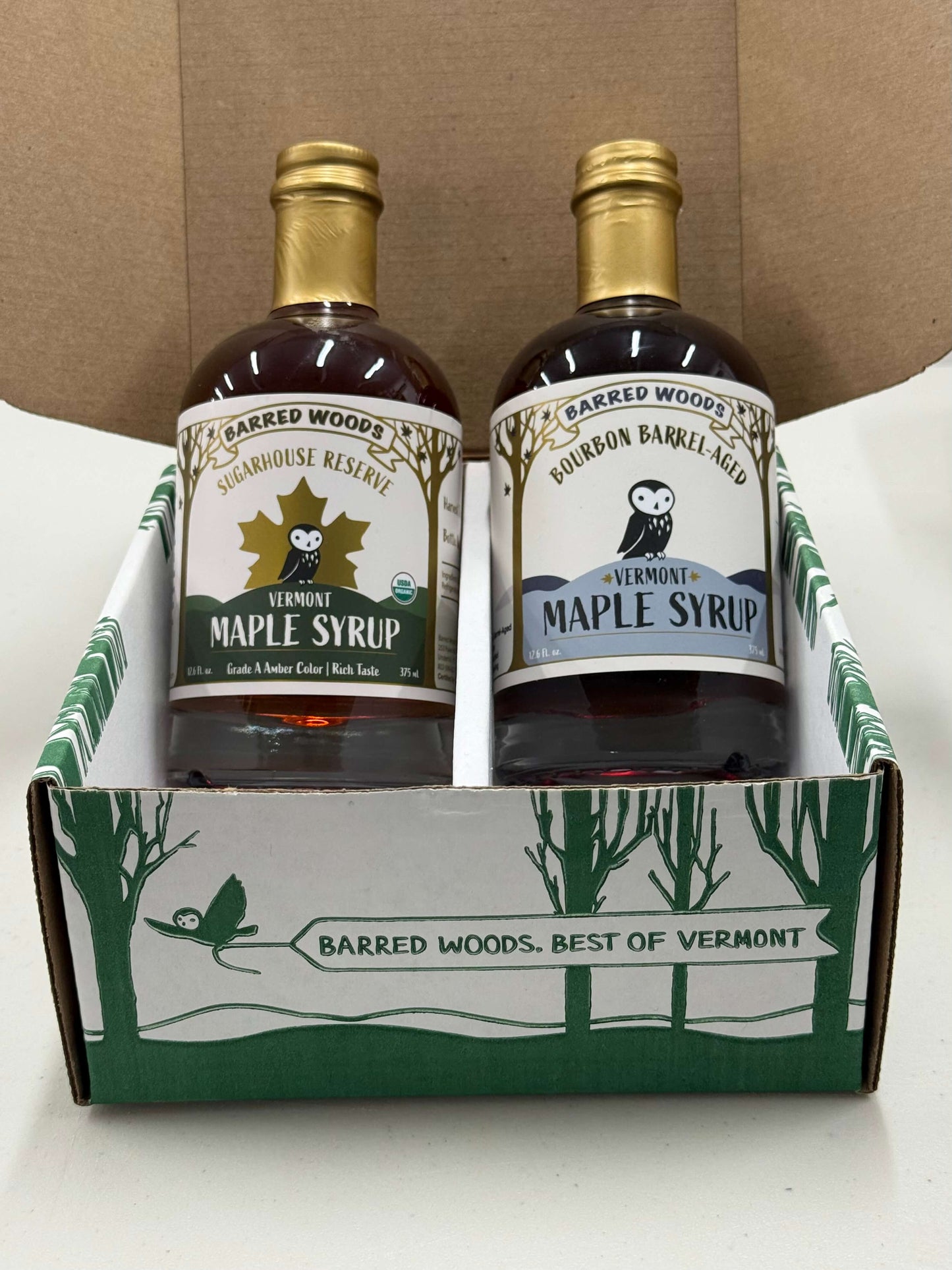 Two bottles of Barred Woods maple syrup in a branded box on a white surface.