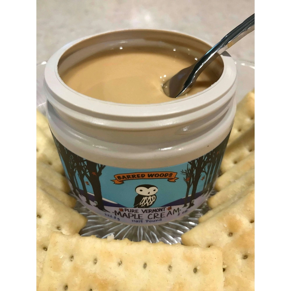 Spoon in jar of creamy Vermont maple spread from Barred Woods surrounded by crackers.   Our maple butter is delicious on toast and bagels also. 